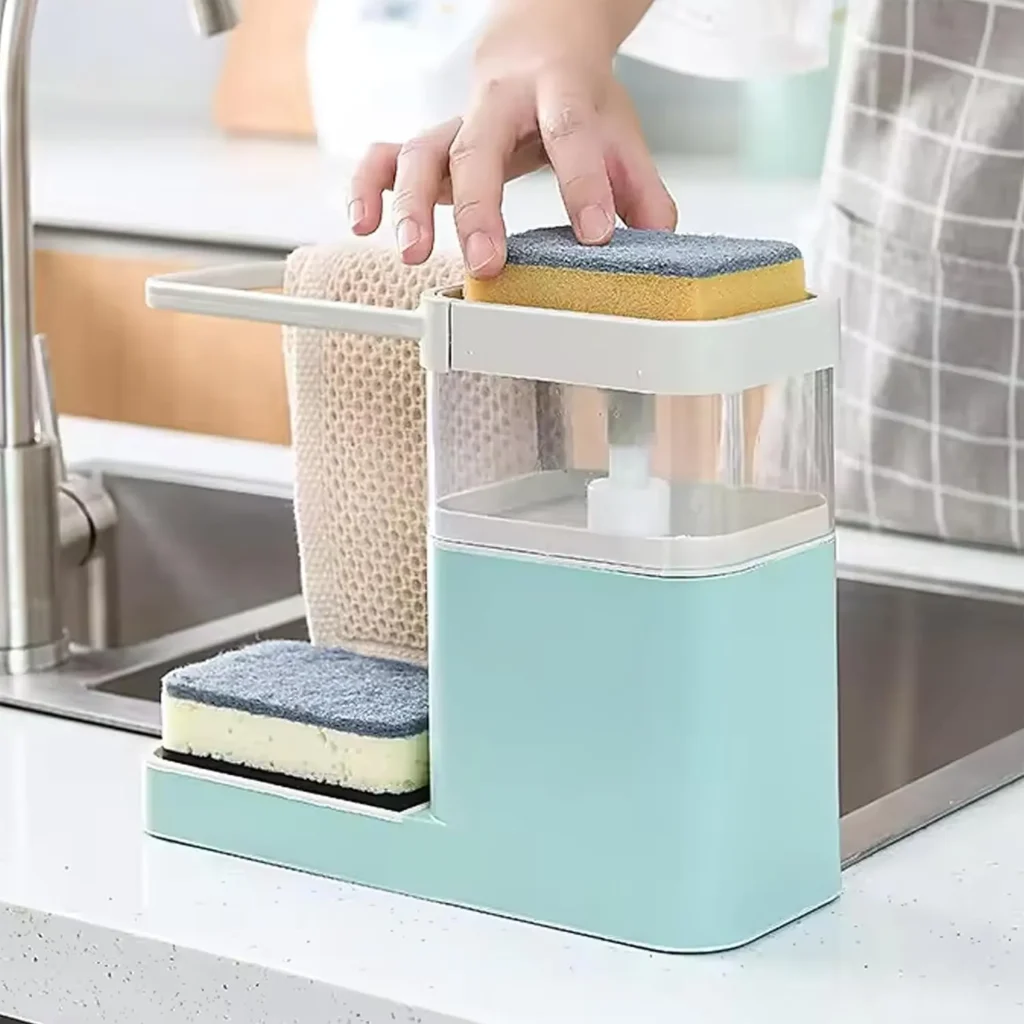 Multifunctional soap dispenser with integrated sponge holder and towel rack placed beside a kitchen sink, promoting convenient and organized dishwashing